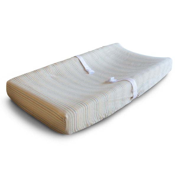 White background with a changing pad, and an Extra Soft Muslin Changing Pad Cover in Retro Stripe by Mushie on it. Retro Stripe is a neutral base with multi colour stripes in retro colours.
