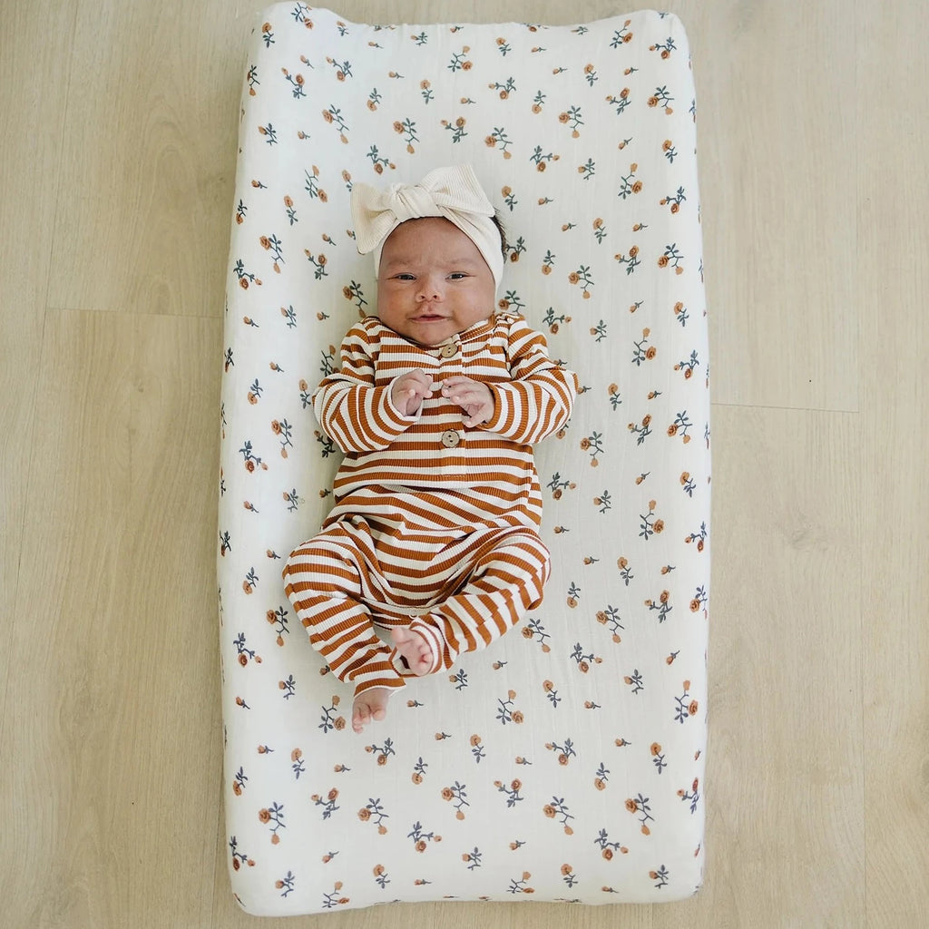 Overhead view of a baby girl laying down on a change oad, with the Cream Floral Changing Pad Cover by Mebie Baby on it.