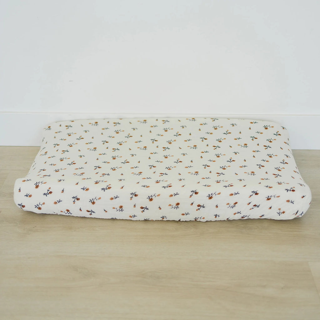 White background with light wood floor and a change pad with the Cream Floral Changing Pad Cover by Mebie Baby on it. Change pad is cream with rust flowers.