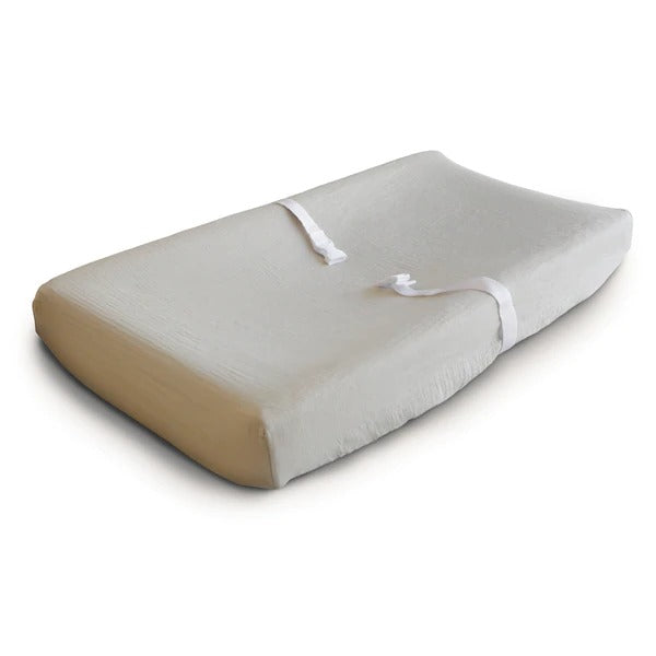 White background with a changing pad, and an Extra Soft Muslin Changing Pad Cover in Fog by Mushie on it. Fog is a cool grey neutral.