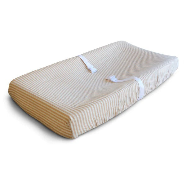 White background with a changing pad, and an Extra Soft Muslin Changing Pad Cover in Natural Stripe by Mushie on it. Natural Stripe is a white with warm beige stripes.