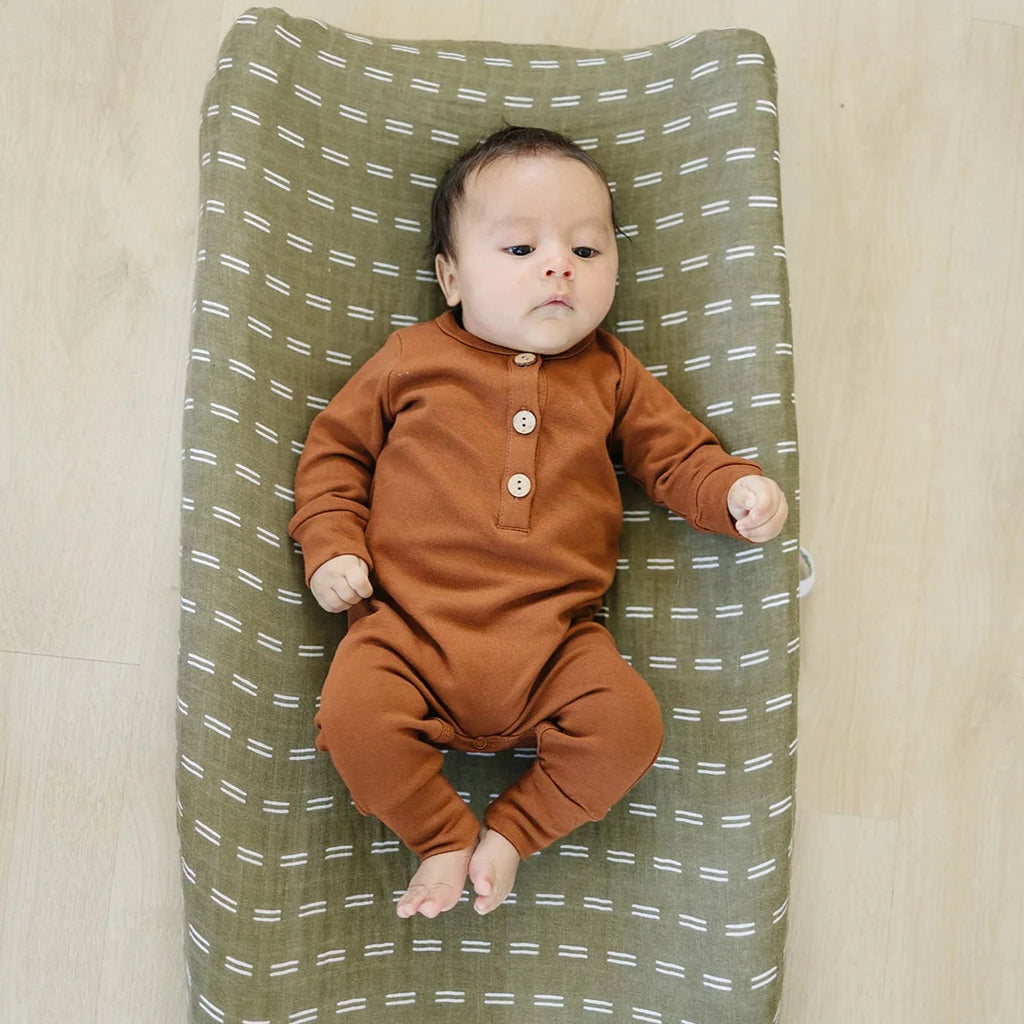 Overhead view of a baby laying on a change pad with the Olive Strokes Changing Pad Cover by Mebie Baby on it.