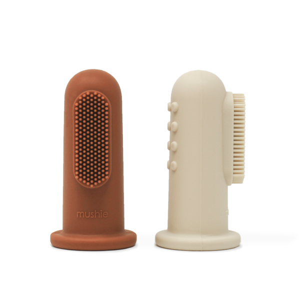 White background with Finger Toothbrush in Clay & Shifting Sand by Mushie. This comes with 2 finger toothbrushes, 1 is a rusty colour, and the other is beige.