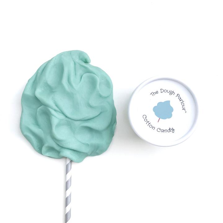 White background with a container of Cotton Candy Play Dough by Dough Parlour, and some play dough molded to look like cotton candy. Play dough is blue, and comes in a white container that says "Cotton Candy" on the lid.