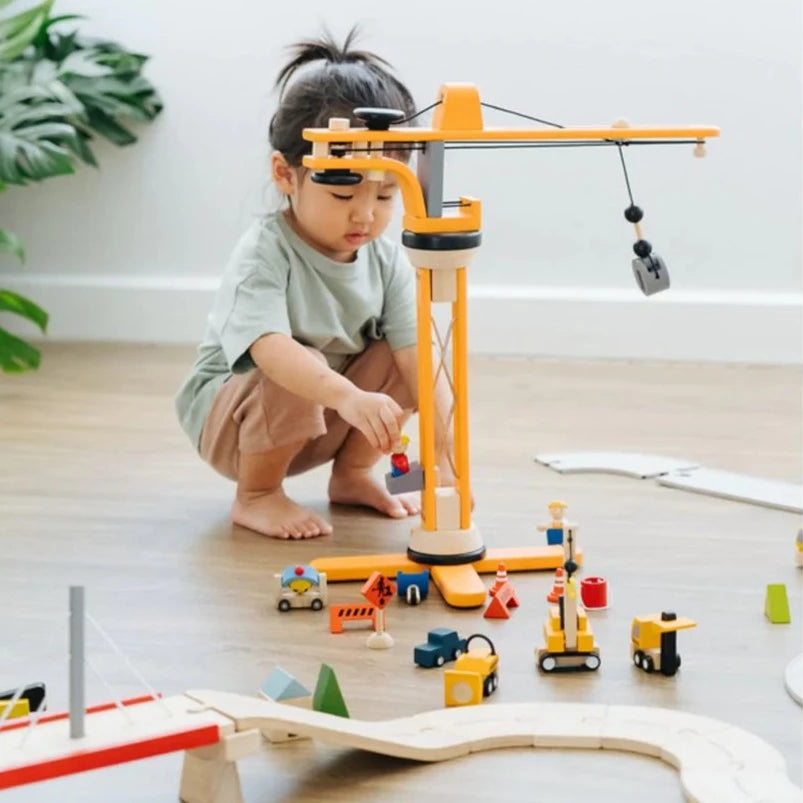 Little girl kneeling down, playing with the Crane Set by PlanToys,