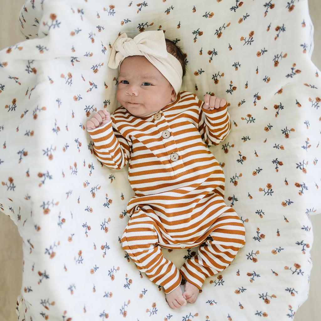 Overhead view of a baby laying in a bassinet with the Cream Floral Muslin Quilt by Mebie Baby behind her.