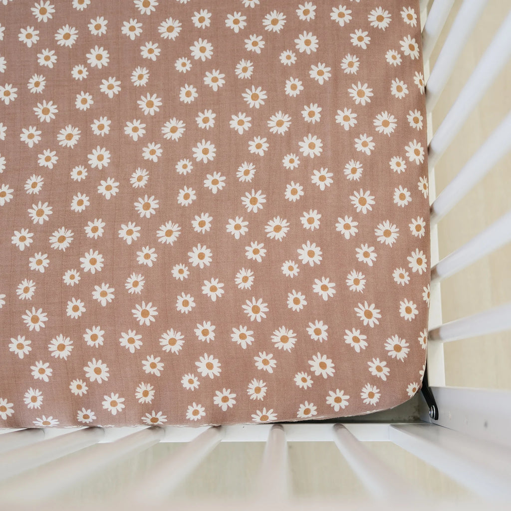 Overhead view of a mattress with the Daisy Dream Crib Sheet by Mebie Baby on it. Crib sheet is a rusty blush colour with white daisies and a rust centre.
