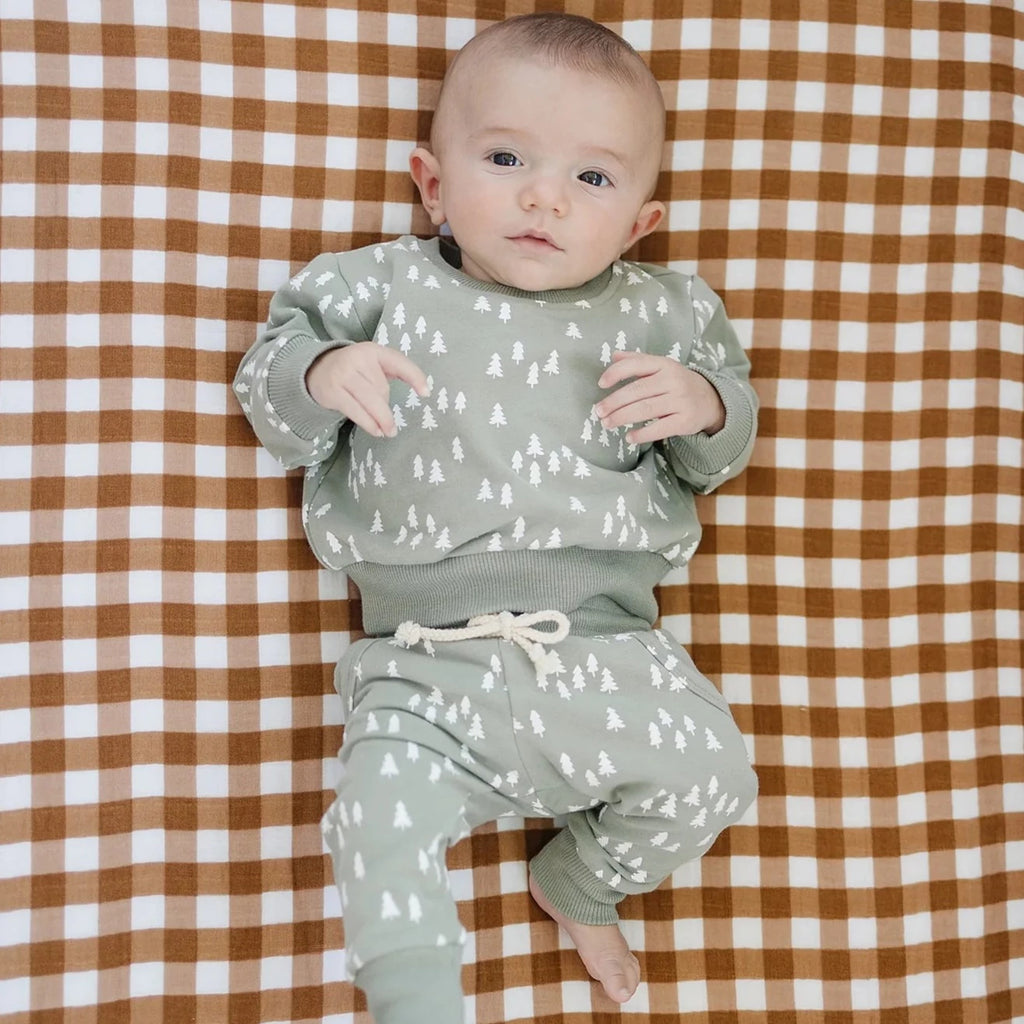 Overhead view of a baby laying on a mattress with the Gingham Crib Sheet by Mebie Baby on it.  Crib sheet is a white and brown gingham pattern.