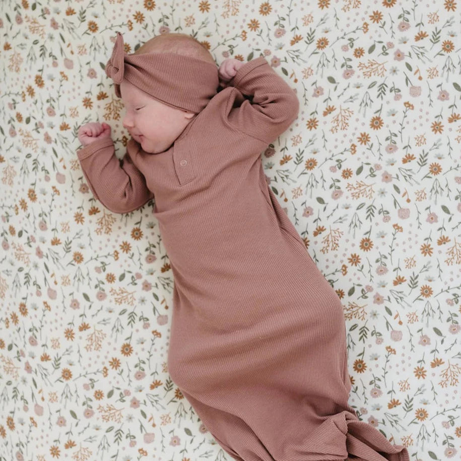 Overhead view of a baby sleeping on a mattress with the Meadow Floral Crib Sheet by Mebie Baby on it. Crib sheet is a light cream colour with rust, sage and pink flowers all over.