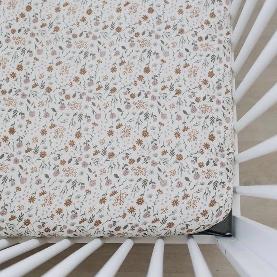 Overhead view of a mattress with the Meadow Floral Crib Sheet by Mebie Baby on it. Crib sheet is a light cream colour with rust, sage and pink flowers all over.