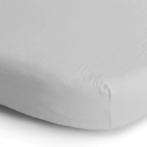White background with a close up of the corner of a mattress with the Extra Soft Muslin Crib Sheet in White by Mushie on it. This is a perfect crisp white colour. 