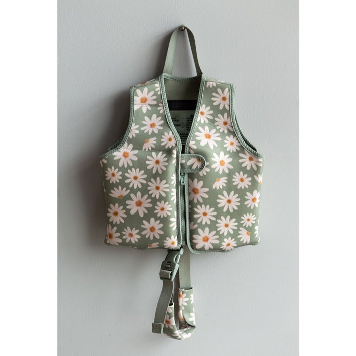 Float Vest in Sage Daisies By Current Tyed Clothing hanging on a nail, on a grey wall. 