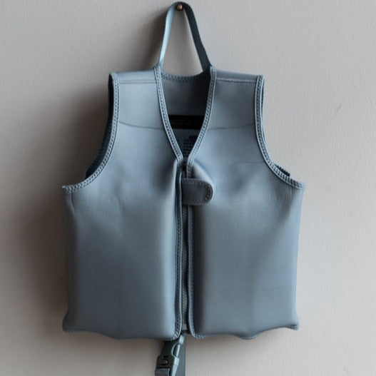 Float Vest in Stone Blue By Current Tyed Clothing hanging on a nail, on a grey wall. 