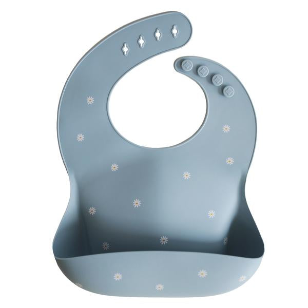 White background with a Silicone Bib in White Daisy by Mushie. Bib is a sky blue colour with white daisies, with a deep pocket on the front, and a rounded neck fastener at the back.