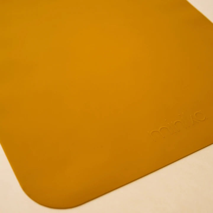 Beige background with a Silicone Placemat in Ochre by Minika. Placemat is square silicone, in an ochre colour.