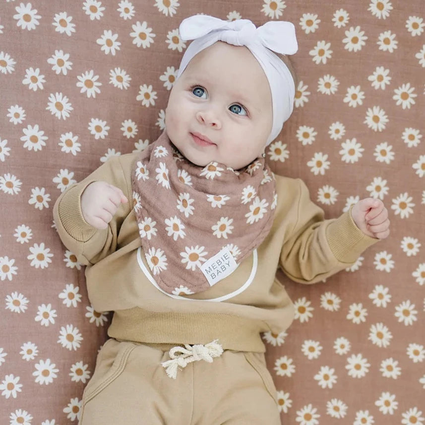 Close up of baby girl laying on daisy dream crib sheet, wearing the Daisy Dream Bib by Mebie Baby.