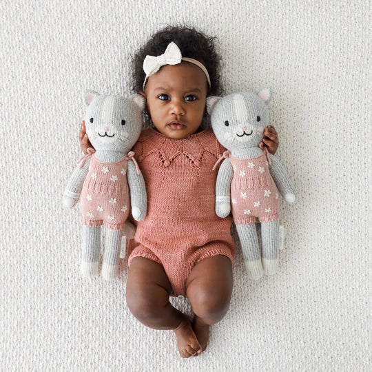 White blanket background with baby girl laying between both sizes of Daisy The Kitten by Cuddle and Kind