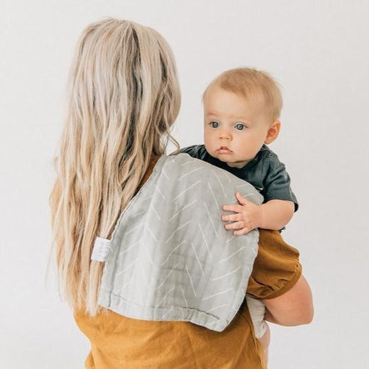 White background with a mama holding a baby, back facing camera, and a Desert Sage Burp Cloth by Mebie Baby draped over her shoulder. Burp cloth is a pale sage colour with white lines all over.