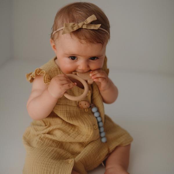 White background with a baby girl chewing on the Dog Teether by Mushie.