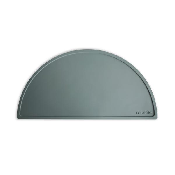 White background with Silicone Place Mat in Dried Thyme by Mushie. Placemat is blue/green silicone in a semicircle.