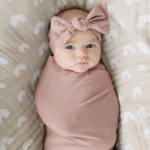 Overhead view of baby laying down, wrapped up snug in a Dusty Rose Stretch Swaddle by Mebie Baby. Swaddle is dusty rose, and is full of stretch.