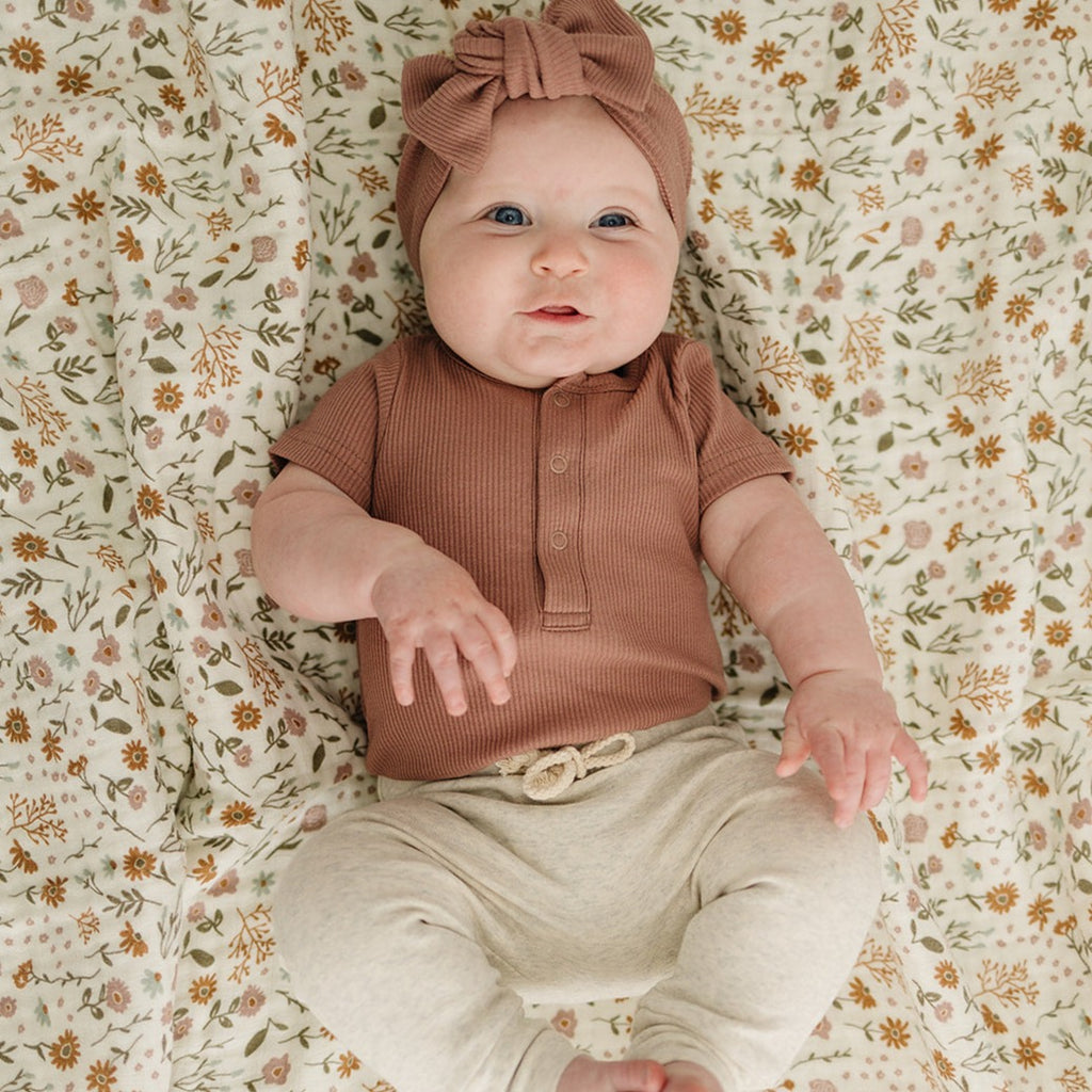 Dusty Rose Bodysuit by Mebie Baby with a matching head wrap, laid on a  floral swaddle by Mebie Baby. 