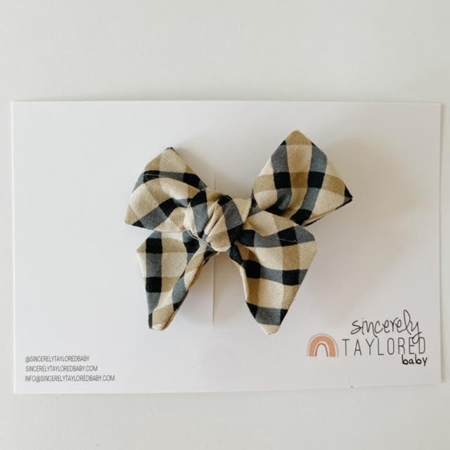 White background with the Fall Tartan Bow by Sincerely Taylored Baby, in its packaging. Bow is a cream/beige/brown/black plaid, on a clip.