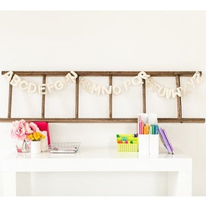 White wall with a ladder decoration, and the Felt Alphabet Garland in White by The Whimsical Woolies hanging.