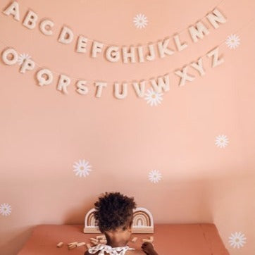 Pink wall with daisy decals all over, and the Felt Alphabet Garland in White by The Whimsical Woolies hanging.