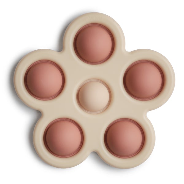 White background with Flower Press Toy in Rose/Blush/Shifting Sand by Mushie. This is a beige colour silicone shaped like a 5 point flower, with 5 rusty rose "pop its" around the outside, and 1 blush in the center.