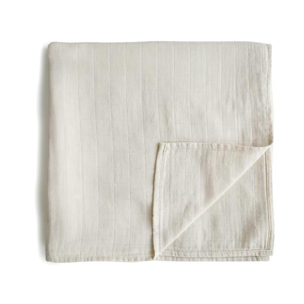 White background with a folded Muslin Swaddle Blanket Organic Cotton in Fog by Mushie. This swaddle is a cream/grey colour.