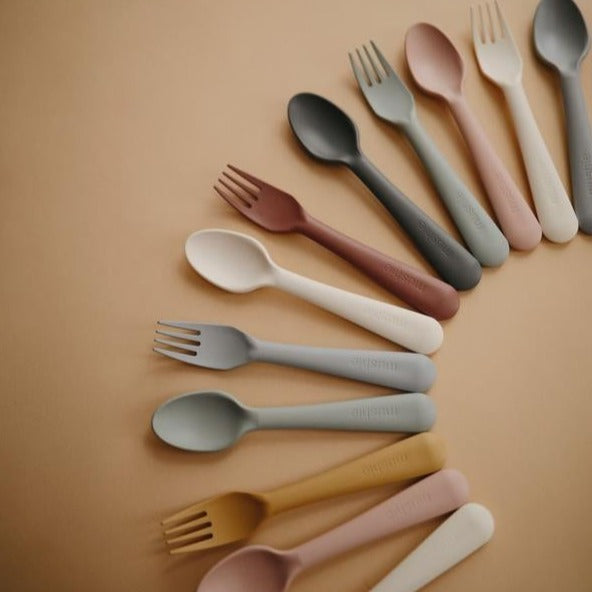 Brown background with Fork and Spoon Sets by Mushie all laid out in an arc shape.