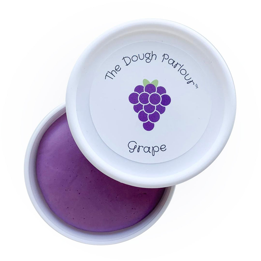 White background with Grape Play Dough by Dough Parlour. Lid is open and set aside, showing the deep purple colour of the dough.
