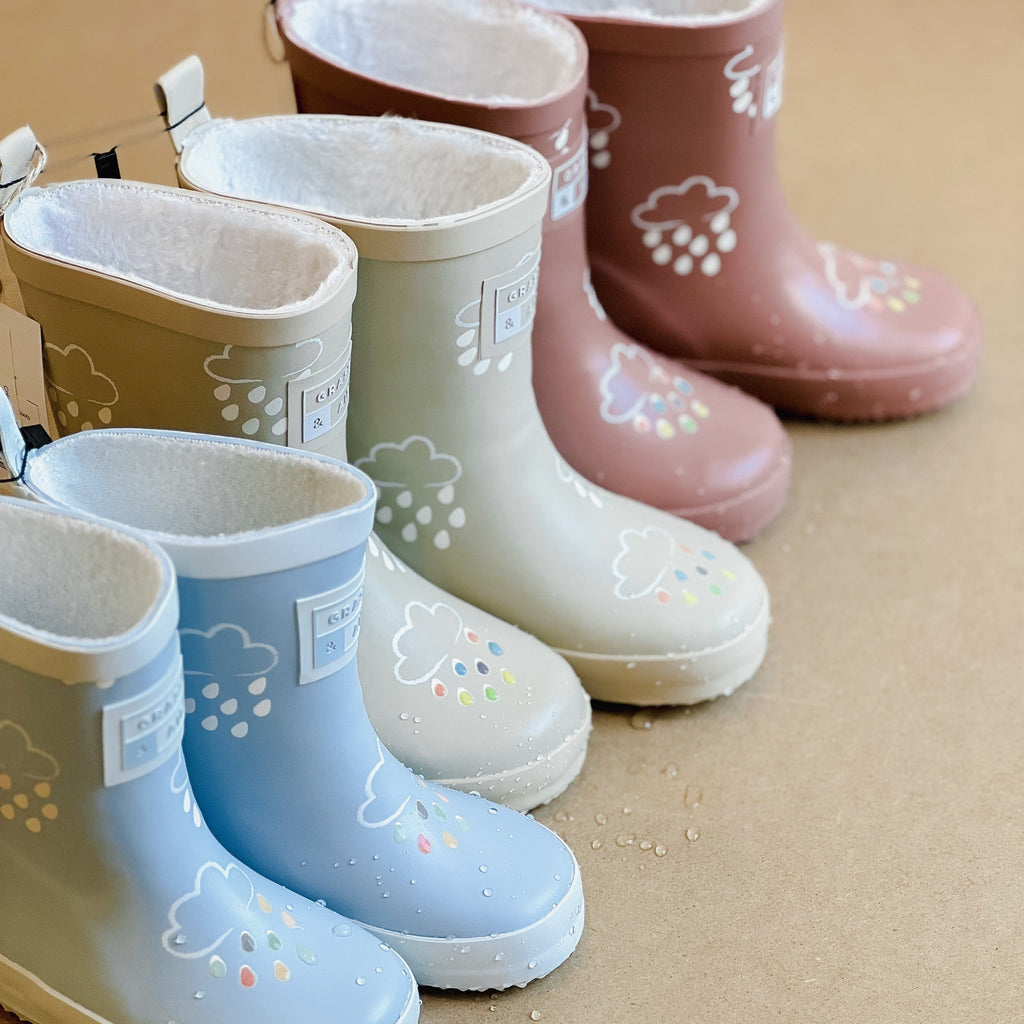 Colour Changing Rain Boots by Grass & Air laid on a beige surface, with water on them. 