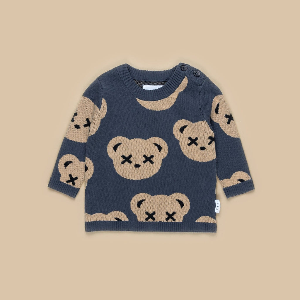 Beige background with Huxbear Teddy Knit Jumper in Ink by Hux Baby. Jumper is navy with light brown bear faces all over, and x's over their eyes.