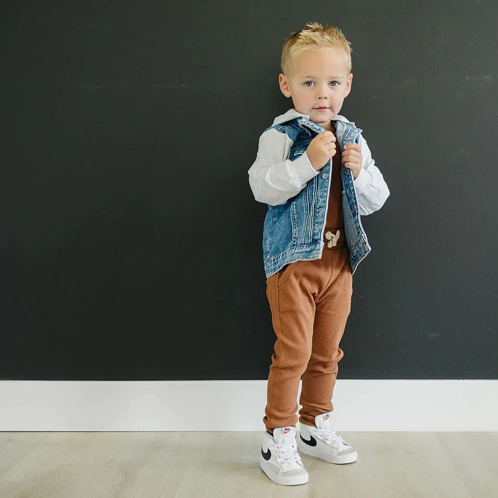 Dark wall with a toddler boy standing wearing a mustard two piece set, and the Mebie Baby Hooded Jean Jacket by Mebie Baby over top.