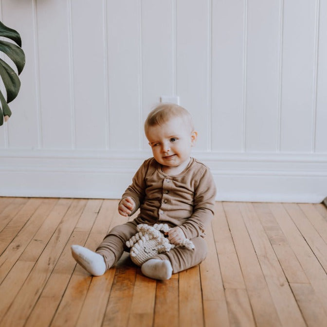 Baby playing with Octopus Rattle in Ivory, on a wooden floor in front of a white wall. 