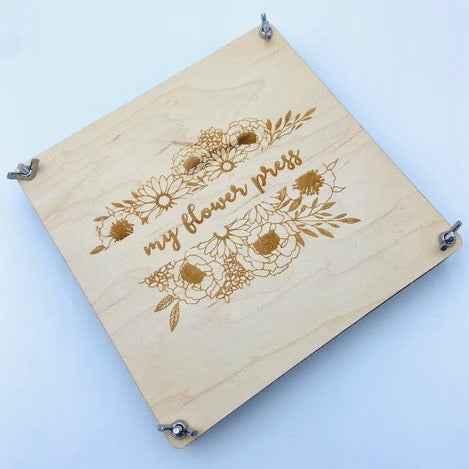 White background with an overhead view of the Flower Press by Concrete Barn. Flower press is a square and says "my flower press" in script on the front, with engraved flowers.
