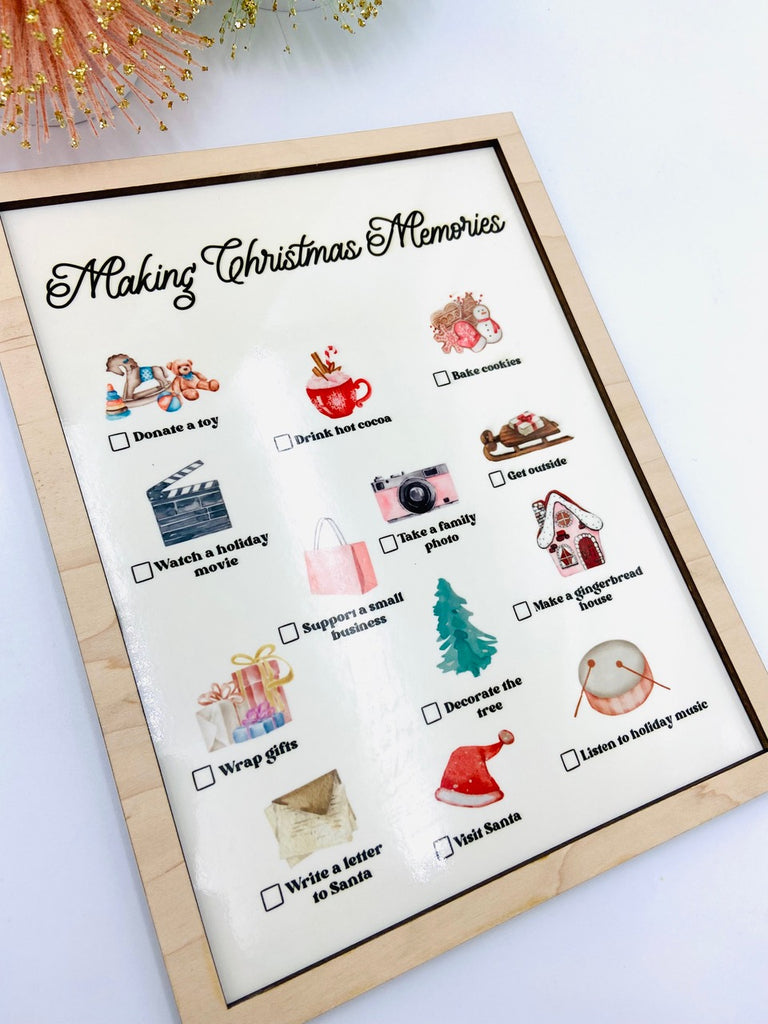 White background with the 'Making Christmas Memories' Dry Erase Board by Concrete Barn. Board has a dry erase base, and it says "Making Christmas Memories" on the top, with pictures and checkmarks all over.