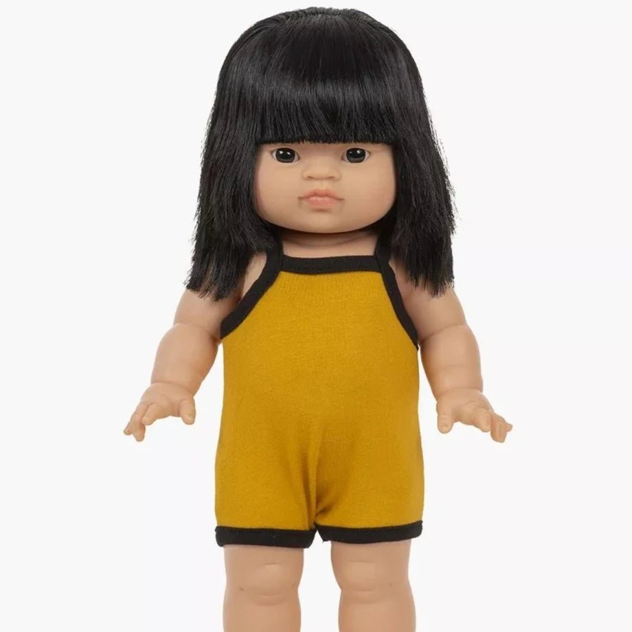 White background with Jade-Lou Doll by Minikane. Doll is an asian girl with dark hair and eyes, wearing a mustard romper with black border.