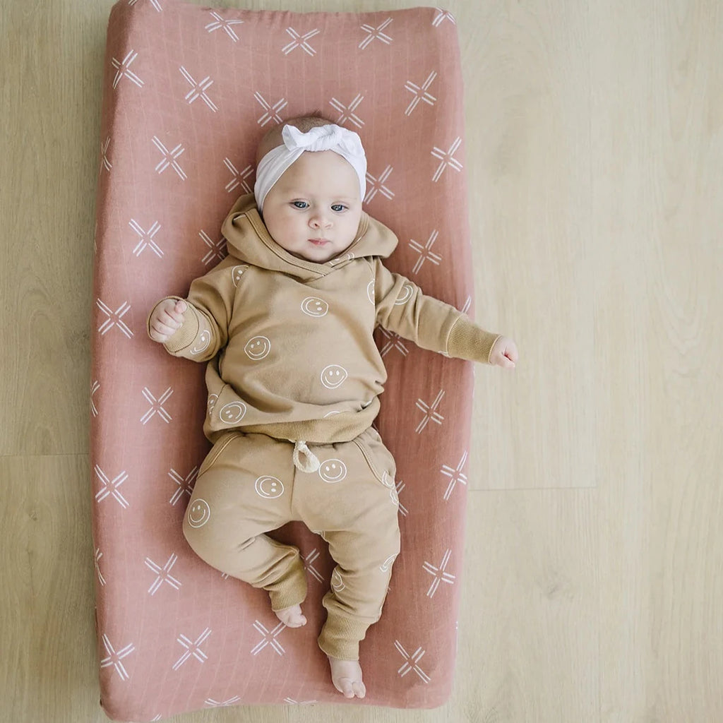 Overhead view of a light wood floor, and a baby girl laying on the Just Peachy Changing Pad Cover by Mebie Baby.