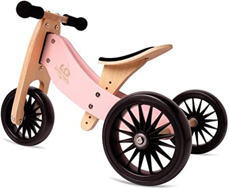 White background with a Tiny Tit Plus Balance Bike in Rose by Kinderfeets. Bike is a natural wood with rose details, black wheels, black handlebars, and a black seat.