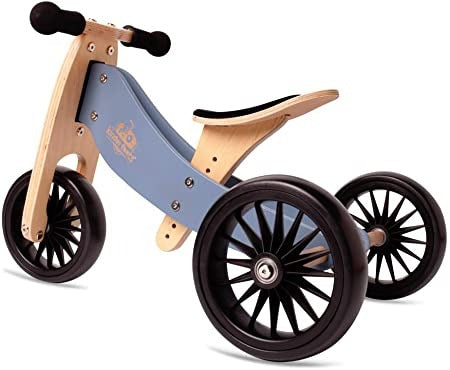 White background with a Tiny Tot Plus Balance Bike in Slate Blue by Kinderfeets. Bike is natural wood with slate blue details, black wheels, black handlebars, and a black seat.