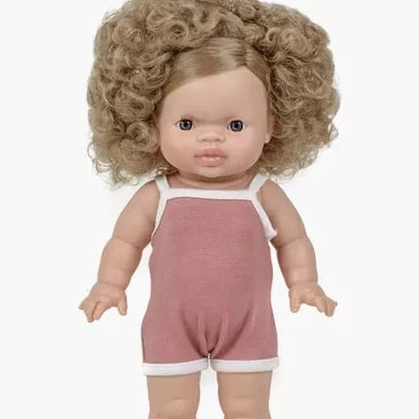 White background with Lise-Anaïs Doll by Minikane. Doll has light skin with dark eyes, and curly blonde hair, wearing a blush colour spaghetti strap romper.