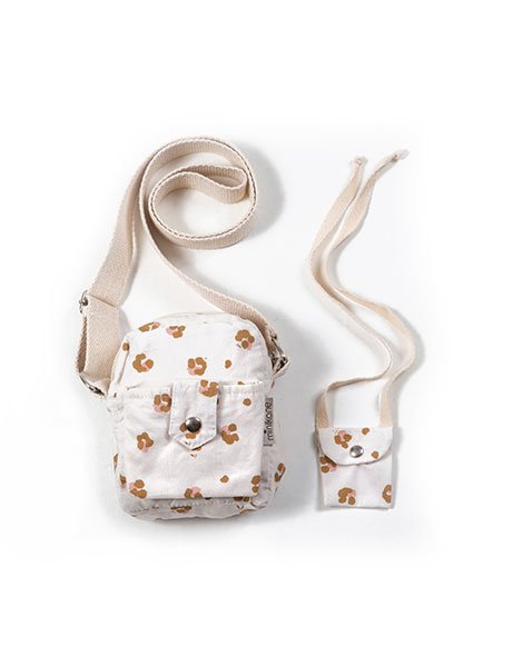 White background with Lola "Holly" Backpack Duo by Minikane. Backpack duo includes 2 bags, 1 for child and a matching for doll, this is white with flowers and a canvas strap.