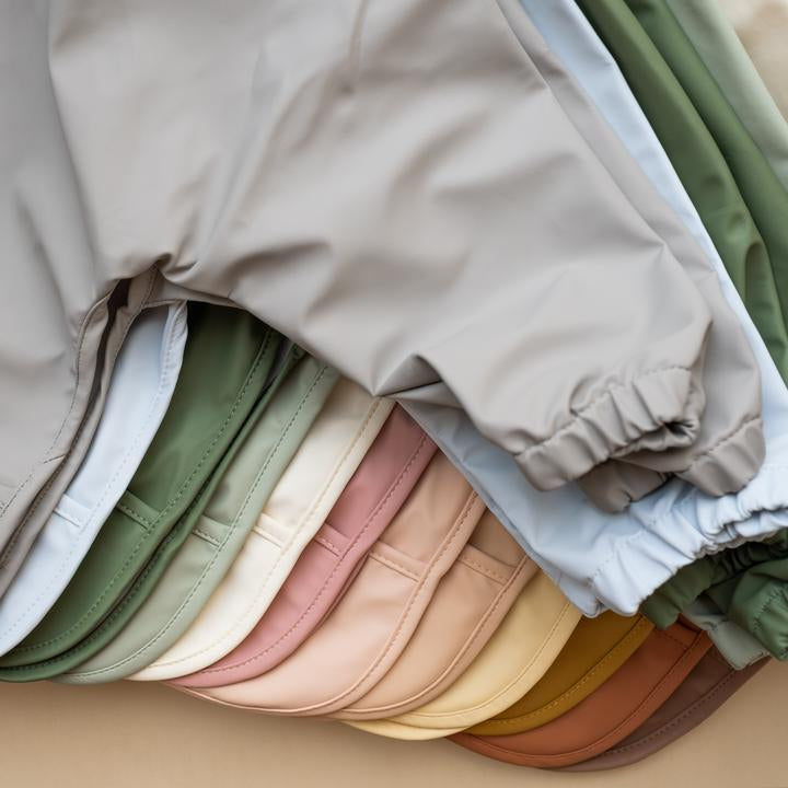 Beige background with a stack of Long Sleeve Bibs by Minika.