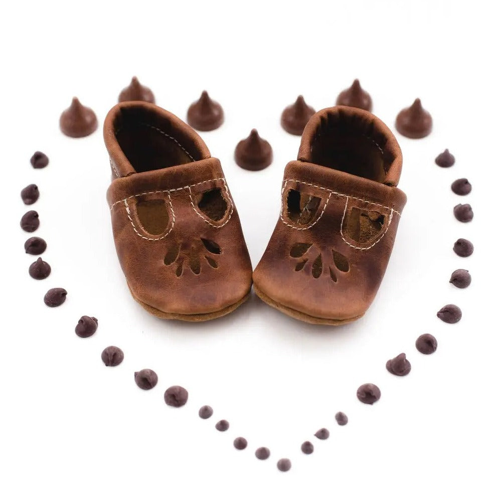 White background with a heart made out of chocolate chips, and the Lotus T-Strap Flats in Brandy by Starry Knight Design in the center. Flats are a warm brown colour.,