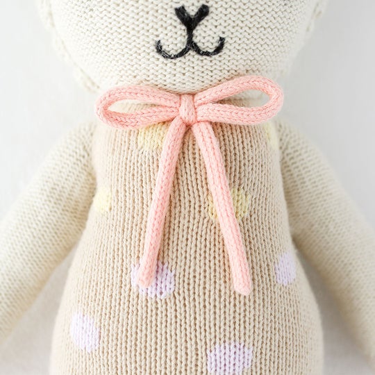 Close up details on Lucy The Lamb (Pastel) by Cuddle & Kind. Showing the knotted bow at the neckline, in pink.