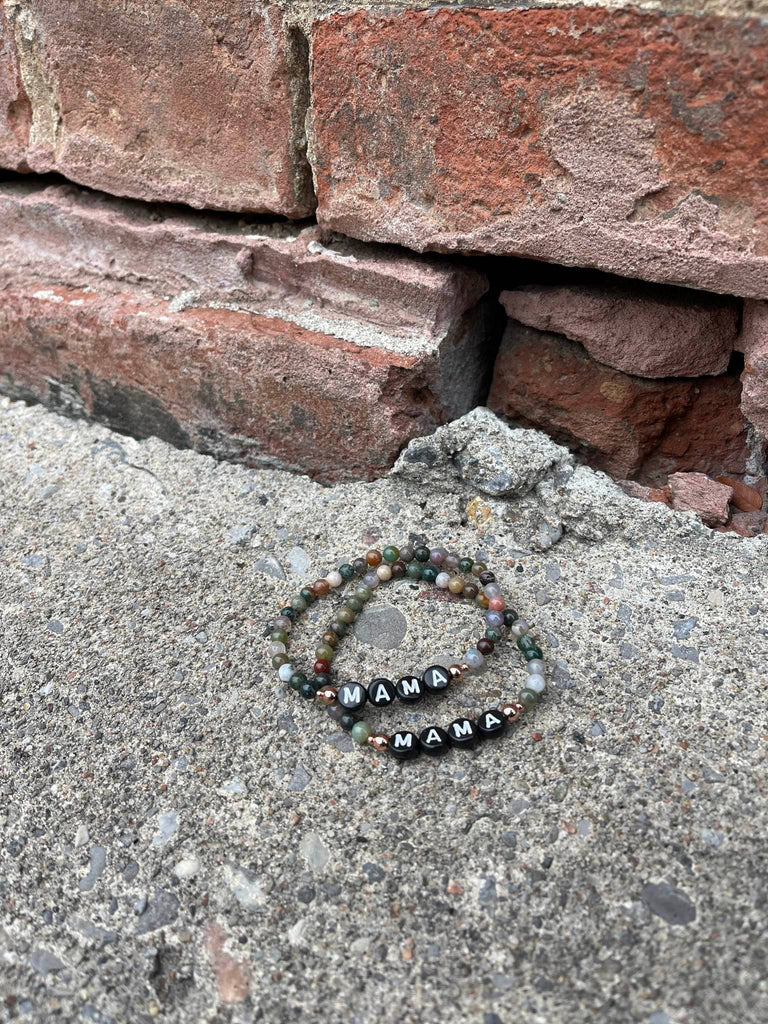 Indian Agate Mama Bracelets by Earth & Ether Co., laid on concrete in front of a red brick wall. 