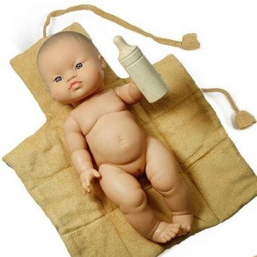 White background with the Changing Mat for Dolls with Bottle by Minikane, and a doll laying on it. Changing mat is an ochre colour, and bottle is made of wood.